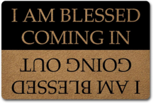 Two-tone sign with the phrase'I am blessed coming in' shown upright on a black section and inverted on a brown section.