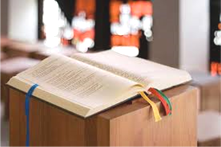 Open Bible resting on a wooden lectern with colorful ribbon bookmarks sticking out.