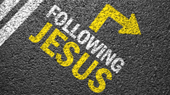 Stencil on pavement reading 'FOLLOWING JESUS' in white and yellow letters with a yellow right-pointing arrow.