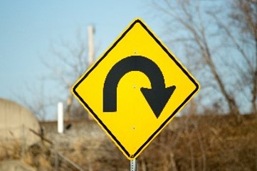 Yellow diamond warning sign with a black U-turn arrow indicating a sharp turn ahead.