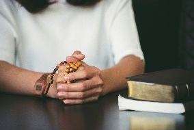 Person's hands are clasped on a dark table, wearing a beaded bracelet and a wristwatch, with two books resting nearby.