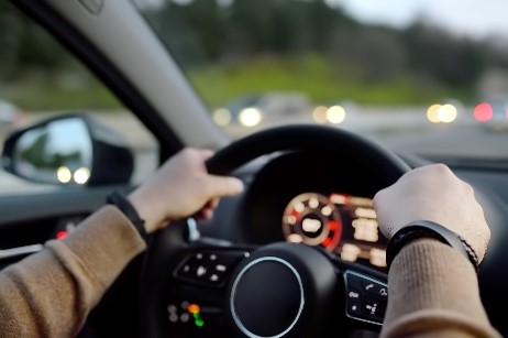 Person's hands gripping a car steering wheel with the dashboard and road ahead blurred.